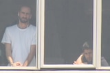 Two men stare out the window of the Mantra Hotel looking into a camera and listening to a reporter interviewing them from inside