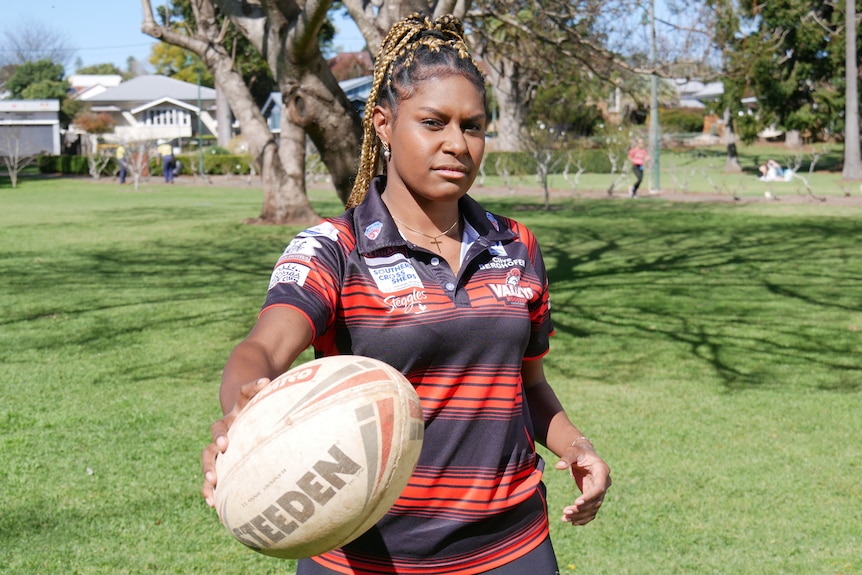 A female First Nations rugby league player on the field, with a ball in her hand