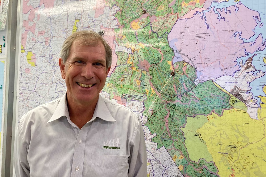 A man wearing a collared shirt stands smiling in front of a map.