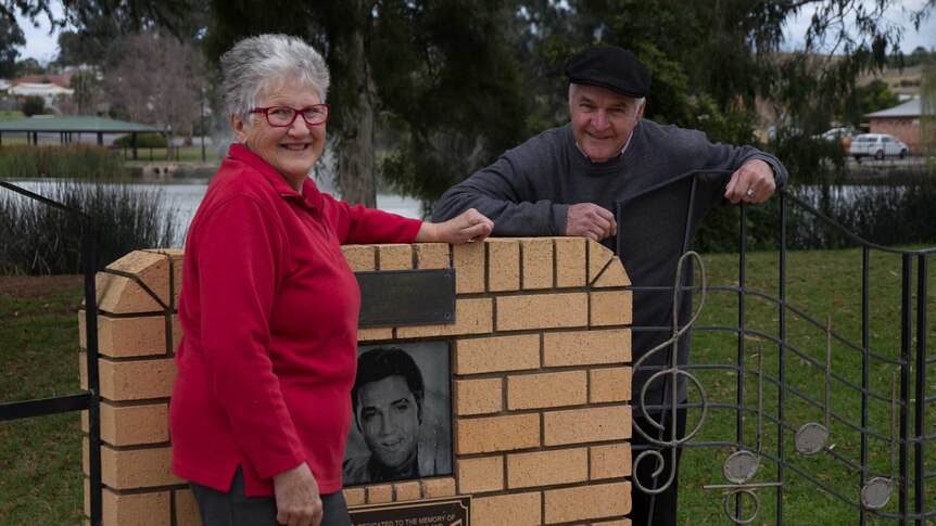 A man and woman standing next to a wall with a picture of Elvis Presley on it and a gate with musical notes on it
