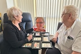 a man and woman sitting at a table looking at a photo of their daughter who died