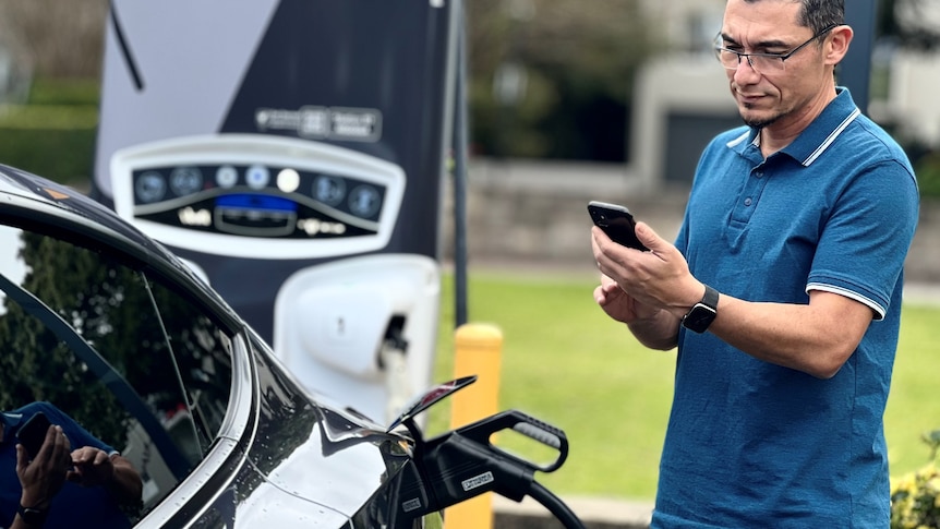 a man on his phone infront of a charging station with his electric car