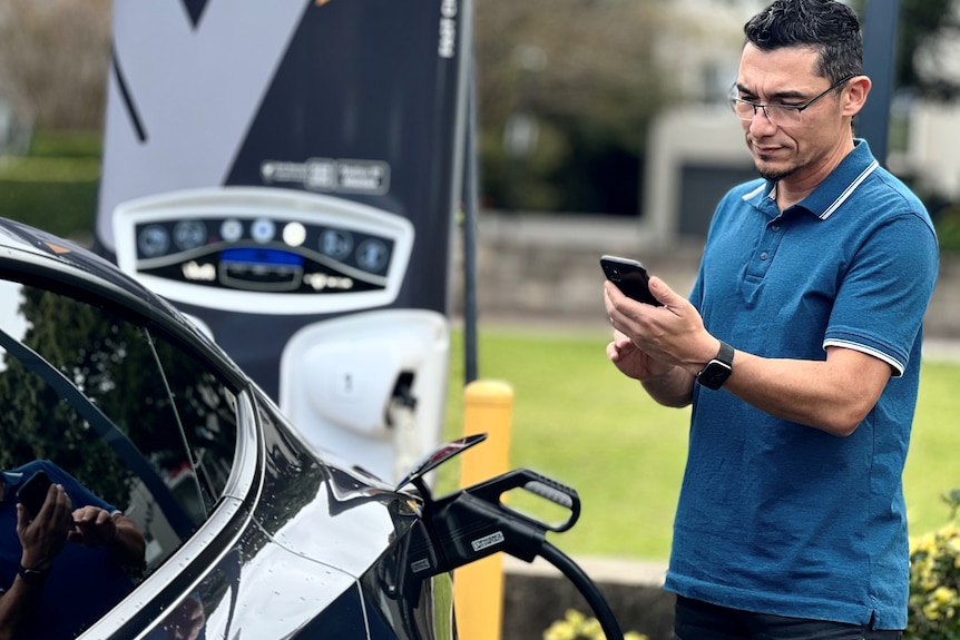 a man on his phone infront of a charging station with his electric car