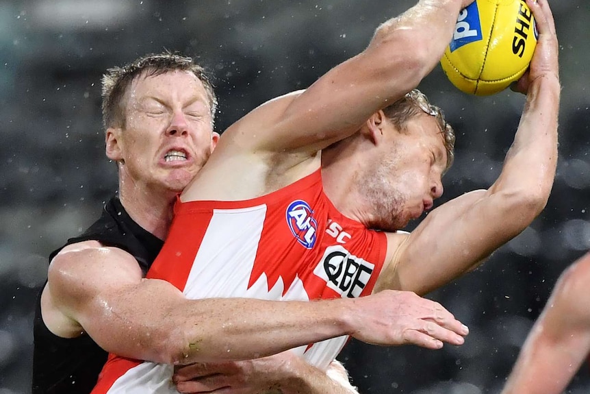 Jack Riewoldt grimaces as he tackles Callum Mills, who lifts his arms and the ball above his head.