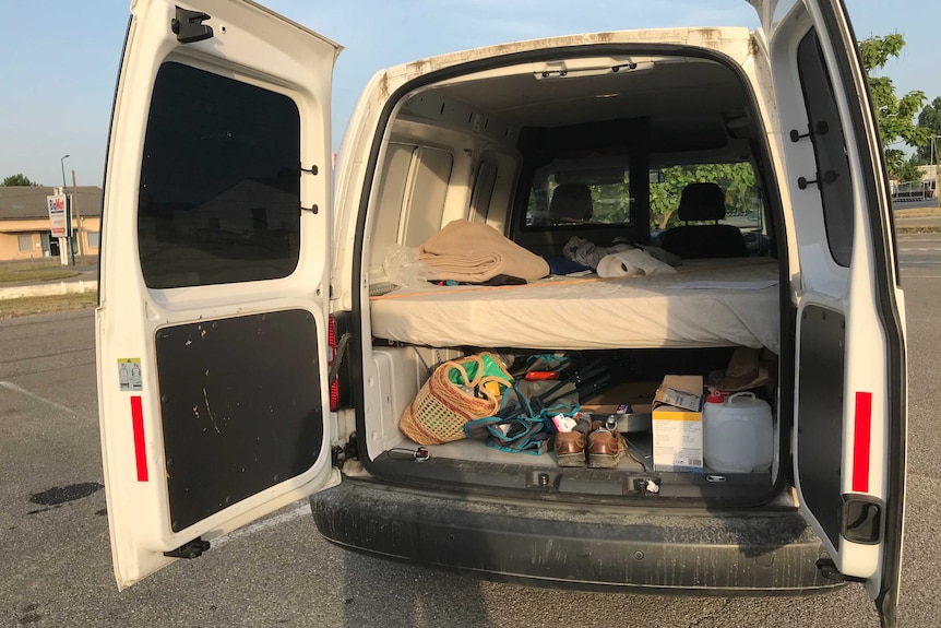 The back of a car doors open showing a mattress and his few belongings.