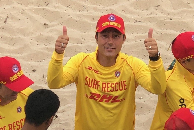 Man in yellow and red lifesaver outfit does thumbs up for the camera