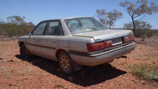 A silver sedan parked on the dirt next to a remote highway in South Australia