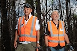 Doug Chang holds a chainsaw and Greg Murphy holds a post driver in burnt Kangaroo Valley bushland.