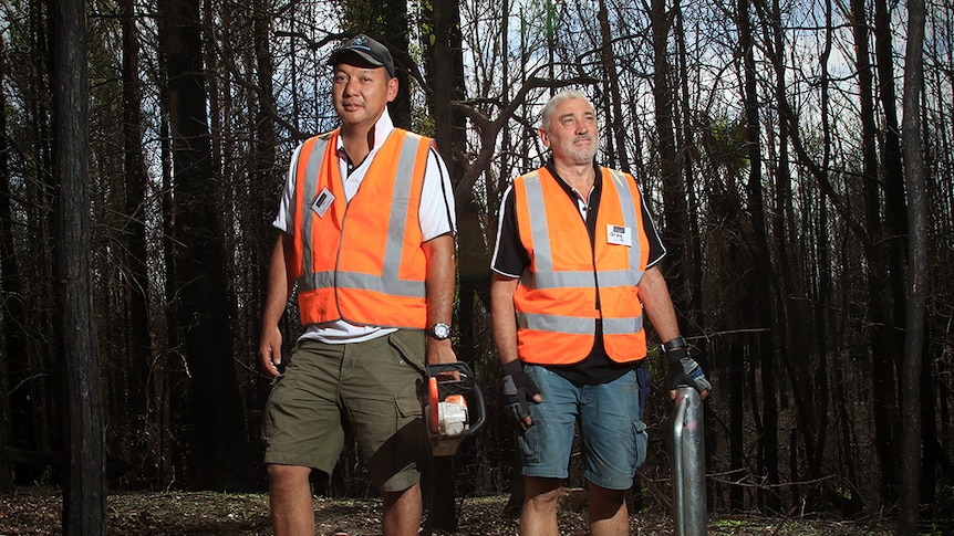 Doug Chang holds a chainsaw and Greg Murphy holds a post driver in burnt Kangaroo Valley bushland.