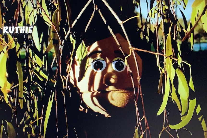 Puppet, half hidden by a gum tree, stares at camera