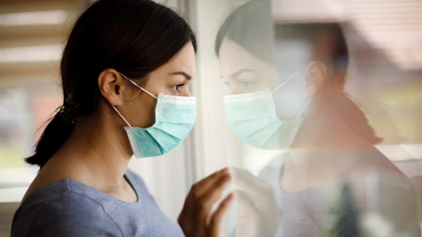 Women wearing a surgical mask looking out of a window.