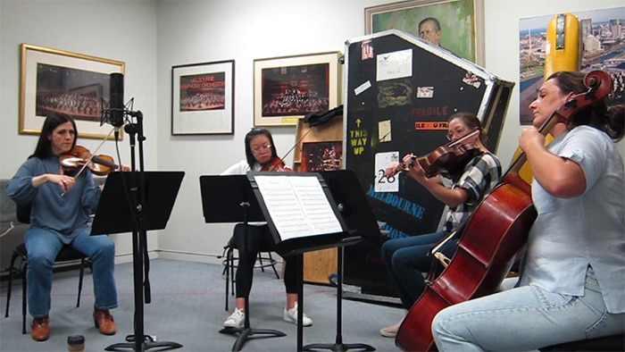 A string quartet perform in a rehearsal room surrounded by artwork and instrument cases.