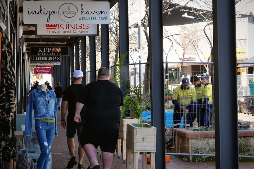 People walk down an outdoor shopping mall, which has been half fenced off for construction work