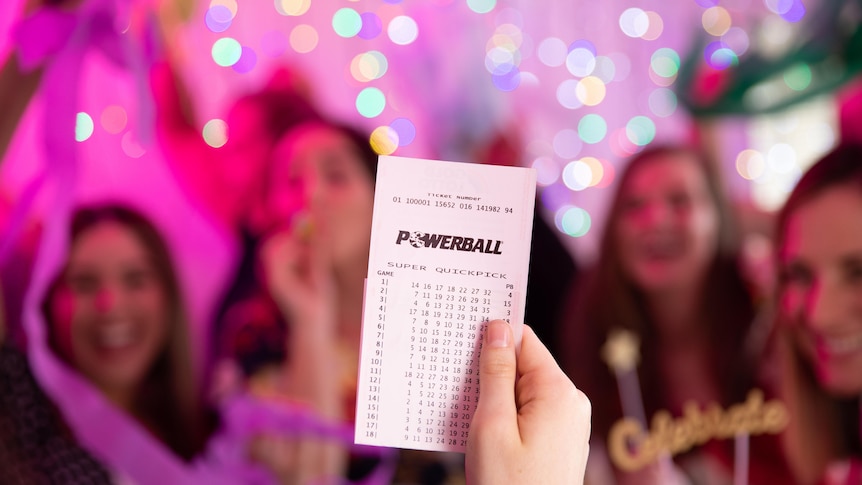 A person holds up a Powerball ticket in front of roomful of people.