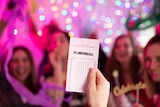 A person holds up a Powerball ticket in front of roomful of people.