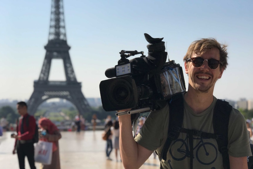 Rothall holding camera on shoulder in front of Eiffel Tower in Paris.