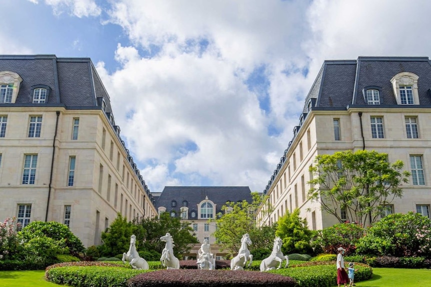 A large grey building similar to the Palace of Versailles near Paris with a sculpture of horses in front.