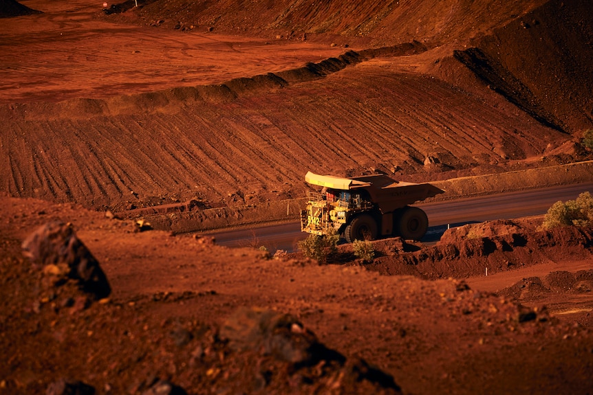 A yellow dump drunk looks tiny surrounded by a big red dirt hole.