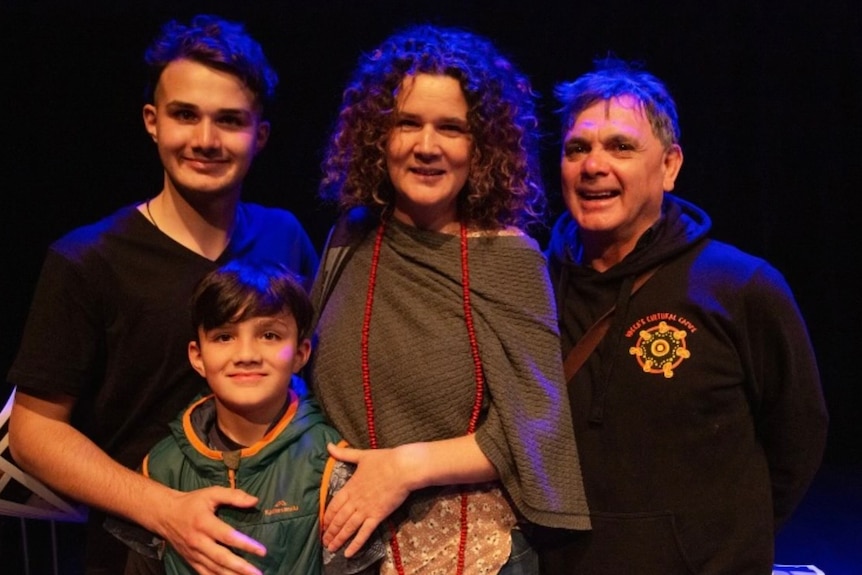 A family of two adults and two kids smile at the camera.