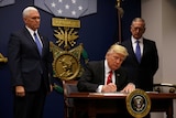 President Donald Trump signs an executive order at a desk