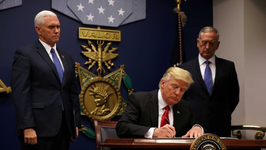 President Donald Trump signs an executive order at a desk