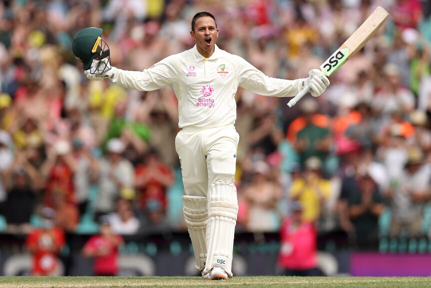Usman Khawaja stands with his arms outstretched with a smile on his face