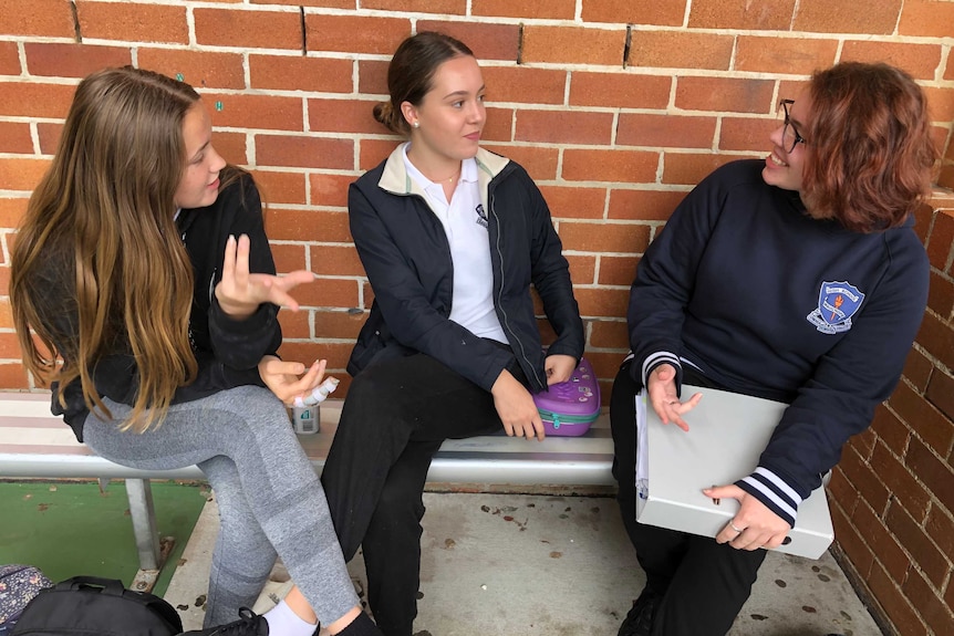 Three female school students chat with each other at school