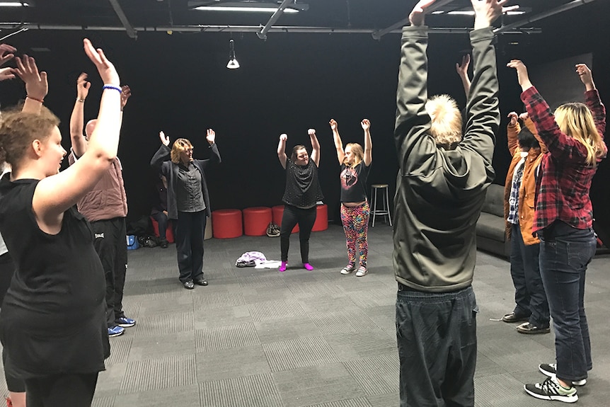 Participants of dance class stand in circle and reach above their heads.