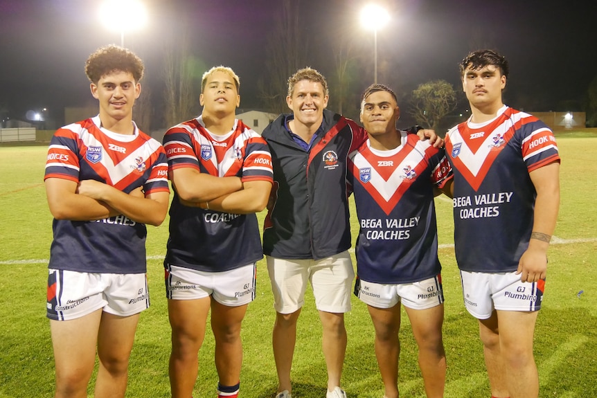 five men in red white and blue sports uniforms stand next to one another on a football field under flood lights