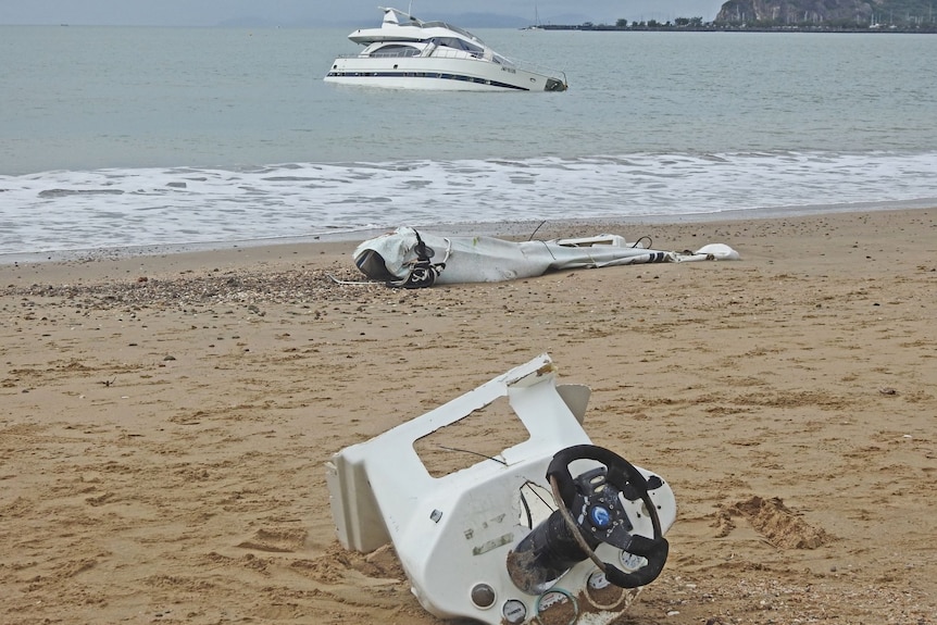 Boat parts washed up on a beach in front of a sunken luxury boat.