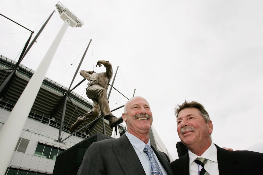 Rod Marsh and Dennis Lillee smile together underneath a large bronze statue of the fast bowler