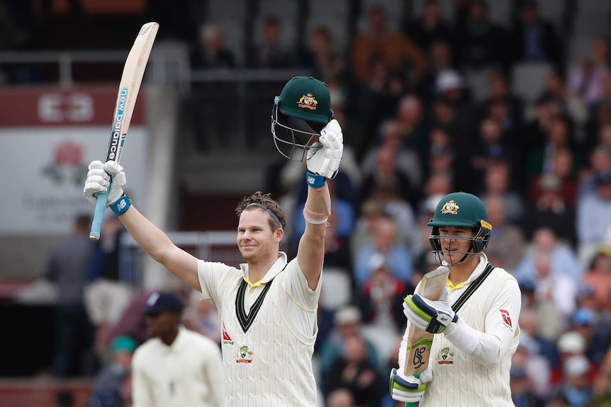 Australia batsman Steve Smith raises his bat and helmet as Tim Paine stands behind him, applauding with his bat.