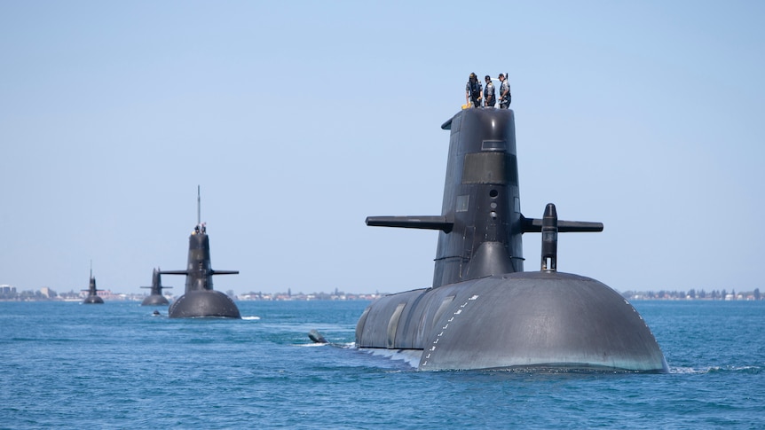 Four submarines half out of the water in the ocean travelling in a line with the closest on the right side of the image