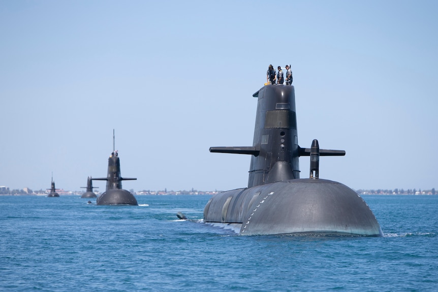 Four submarines half out of the water in the ocean travelling in a line with the closest on the right side of the image