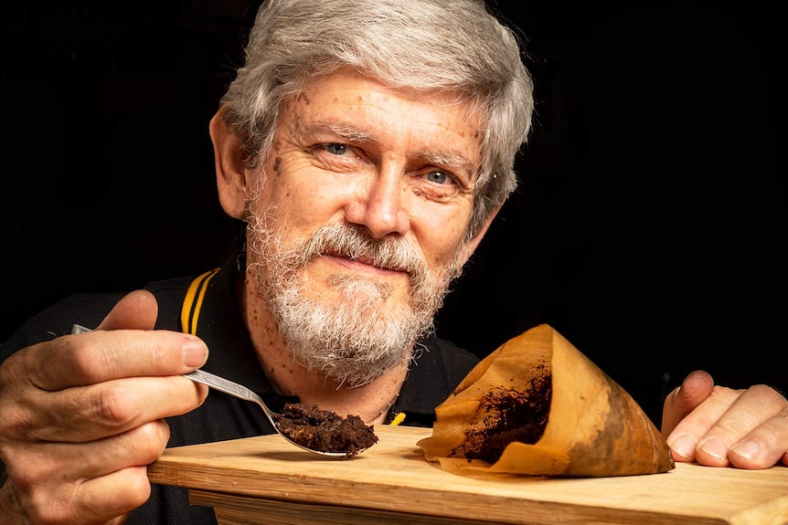 Professor Lindsay Brown holds a spoon with coffee grounds scooped out of a paper bag.