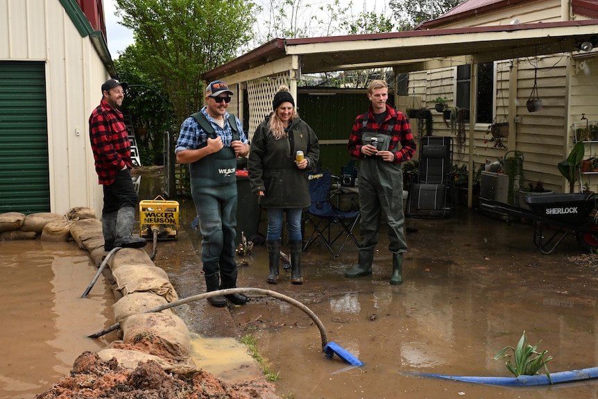 Four people stand around in gumboots looking at muddy water that has flooded the surroundings of their house in Victoria