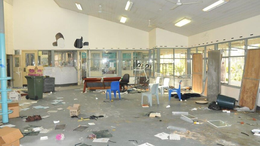 Debris lies scattered around a room at Greenough Regional Prison, including paper, boxes, chairs and bins, with holes in a wall.