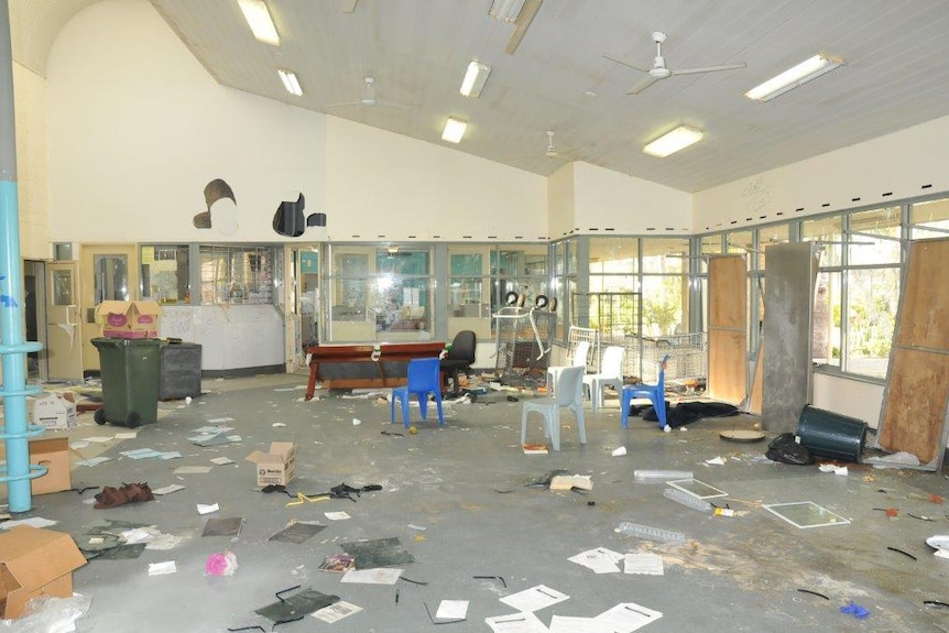 Debris lies scattered around a room at Greenough Regional Prison, including paper, boxes, chairs and bins, with holes in a wall.