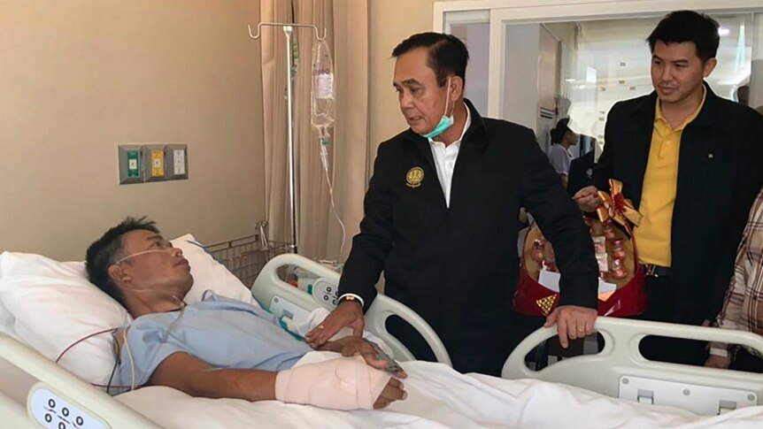 Thailand's Prime Minister Prayuth Chan-ocha stands at the bedside of a patient in hospital.