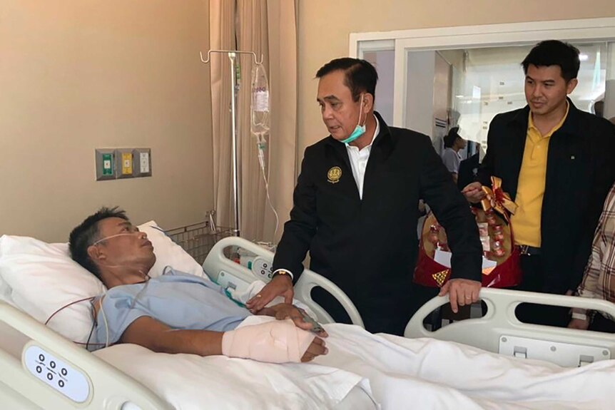 Thailand's Prime Minister Prayuth Chan-ocha stands at the bedside of a patient in hospital.