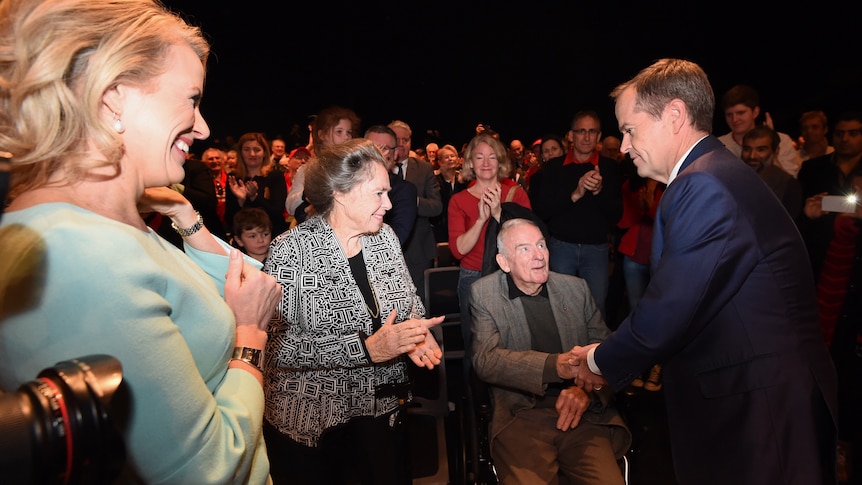 bill shorten shakes hands with hayden, seated, as a crowd looks on