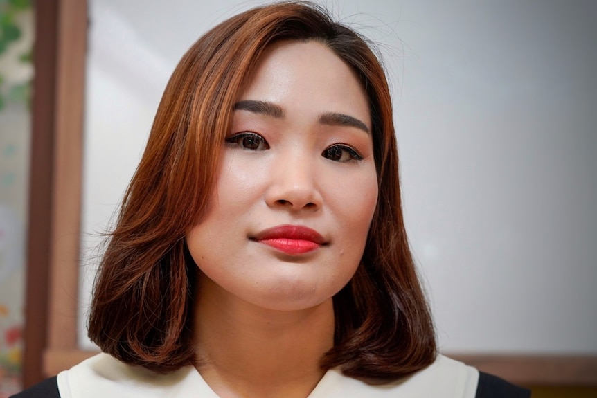 A young Korean woman with bright pink lipstick looks wistfully at the camera
