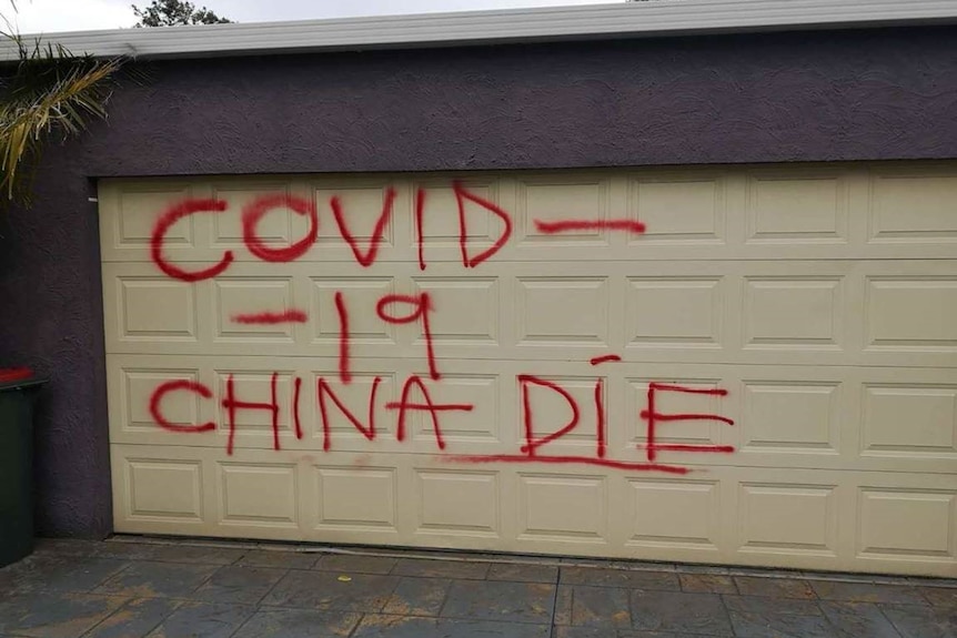 The words 'COVID-19 CHINA DIE' are spray painted in red on a garage door