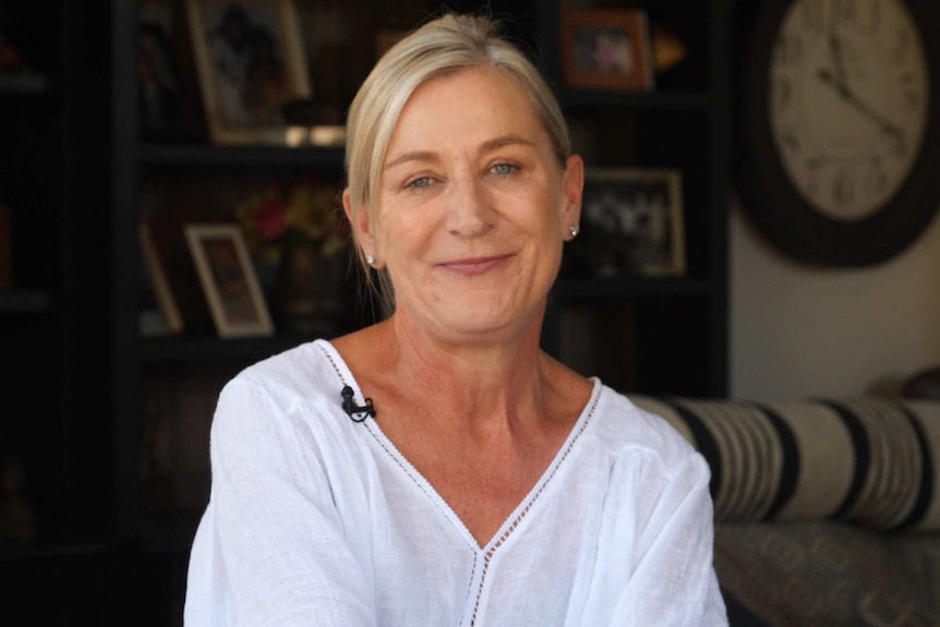 A woman with blonde hair in a white shirt smiling for the camera.