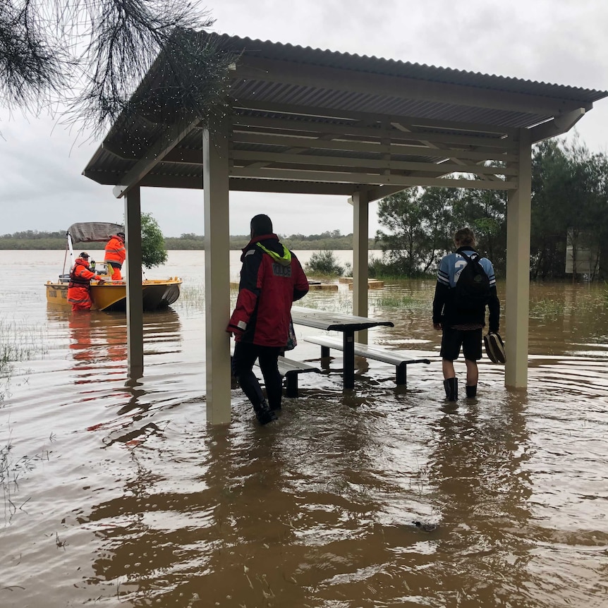 Rescuers in boat and two men standing under picnic table shelter in knee-deep water.
