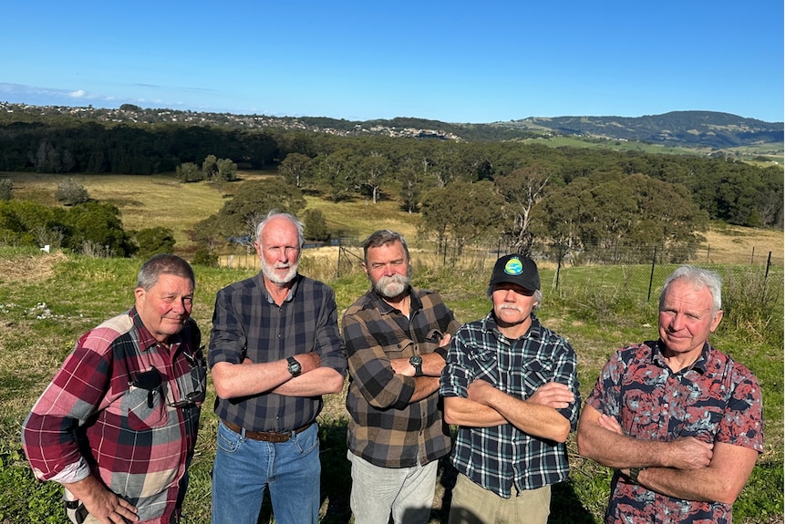 Five men stand on the side of  hill  with their arms folded