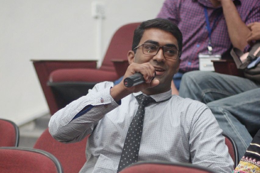 A young man sits in a chair and holds a microphone.