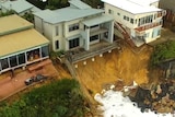 A home rests right on the edge of a long drop off caused by severe erosion of the sand underneath it.