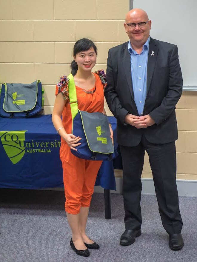 A Chinese student holding a CQU bag stands beside CQUniversity associate vice chancellor Andy Bridges