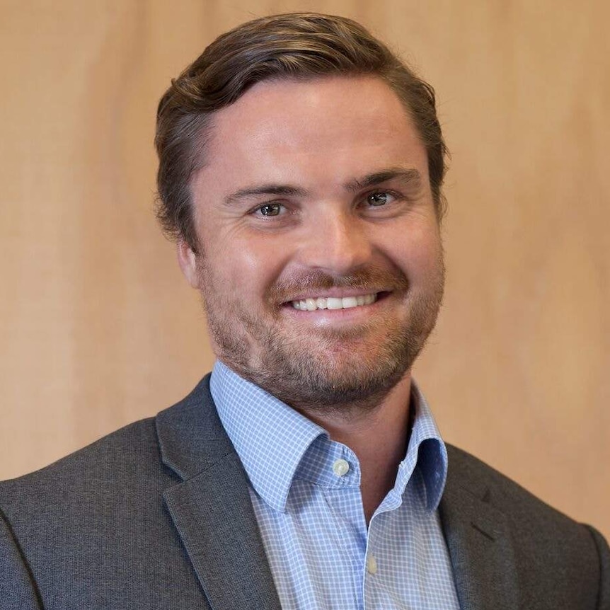 Headshot of a youngish man in a suit looking professional and smiling